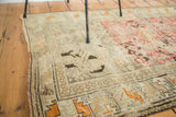 Distressed antique Caucasian rug corner with geometric patterns in ivory, charcoal, and muted orange.
