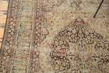 Distressed antique Lavar Kerman rug with dark floral medallion, faded saffron ground, and exposed foundation.