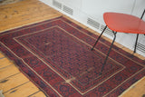 Vintage Belouch rug: allover floral pattern on navy, brick red geometric border, visible wear.