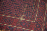 Localized wear on vintage Belouch rug, showing geometric floral field and brick red border.