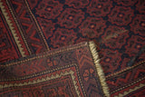 Hand-knotted Belouch rug corner, showing brick red geometric floral border and ivory fringe.