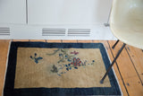 Antique Peking rug corner: beige gold field, dark indigo border, delicate floral tendrils.