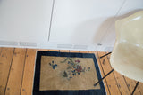 Beige-gold field of the antique Peking rug with blossoming florals, butterflies, and indigo border.