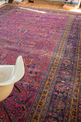 Distressed burgundy plum field of vintage Meshed rug featuring palmettes and ornate dark blue border.