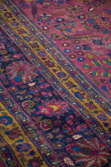 Distressed vintage Meshed rug detail showing scrolling vines, blossoming palmettes, and lotus flowers in plum and navy.
