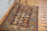Distressed antique Caucasian rug corner, geometric borders in tangerine orange and indigo blue.