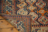 Distressed antique Caucasian rug corner, geometric borders, tangerine, indigo, exposed foundation.