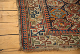 Corner detail of an antique distressed Caucasian rug, featuring colorful geometric borders and exposed foundation.