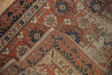 Distressed antique Caucasian rug detail: brick red field, splayed floral motifs, and geometric border.