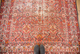 Vibrant distressed vintage Malayer runner with red and orange Herati design, seen with feet.