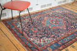 Vintage Persian rug corner detail with geometric and curvilinear floral patterns in blue, red, aqua.