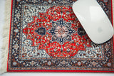 A white computer mouse rests on an ornate cherry red Heriz mouse pad.