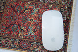 White mouse on a Persian rug mouse pad with red, teal, and gold floral pattern.