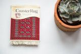 Packaged Bokhara CoasterRug with saturated red field, elephant footprint design, and white fringe.