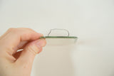 Hand holding the small antique mirror's thick green beveled edge with wire.