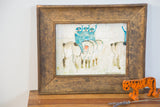 Vintage folk art painting in thick gold frame, showing blue figures and 'Handmom' signature.