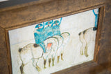 Angled view of vintage folk art painting with blue figures and a rustic wood frame.