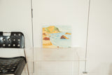 Mid Century Seascape Painting showing light blue ocean, sandy shore, and rocky golden cliffs.