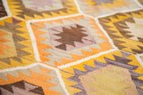 Close-up of vintage Kilim flatweave rug with geometric yellow, orange, lavender, and brown patterns.