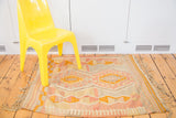 Vintage Kilim rug with faded pink, yellow, grey geometric patterns and fringed right edge.