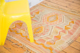 Faded pink, yellow, and grey geometric design on vintage Kilim rug with fringed edge.