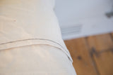 Natural canvas pillow back with black zigzag stitching, showing the envelope closure.
