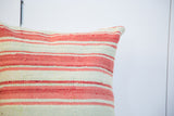 Corner of striped kilim pillow, showing faded red and light green woven texture.