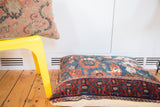 Antique Lilihan floor pillow featuring a richly patterned red border and dark blue field, with golden backing.