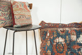 Antique Persian rug floor pillow featuring dark blue, red, and green geometric pattern with aged texture.