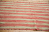 Close-up of vintage Moroccan Kilim flatweave with coral red and pale green stripes and fringe.