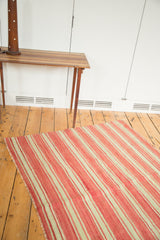 Detail of vintage Moroccan Kilim flatweave showing coral and pale green stripes with a fringed edge.