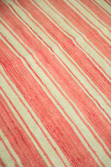 Textured flat weave of a vintage Kilim rug showing coral and cream diagonal stripes.
