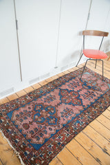 Vintage Malayer rug close-up: blush rose field, blue tribal motifs, tattered fringe.