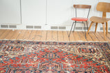 Distressed vintage Heriz carpet's rectlinear patterns, rich red, navy, ivory tones, tattered fringe.
