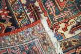 Distressed vintage Heriz rug detail with secured red selvedge, tattered fringe, and rich geometric patterns.