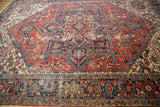 Decorative distressed Heriz carpet featuring navy, red, ivory, and rectilinear patterns.