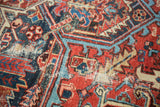 Detailed view of a vintage Heriz carpet's distressed rectilinear design in rich reds and blues.