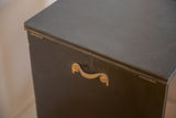Close-up of antique bureau's dark wood surface with ornate brass scroll handle.