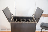 Open top of dark antique hidden bar revealing circular bottle compartments.