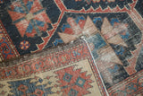 Distressed vintage Bakhtiari rug corner with indigo, madder red, and beige pile and foundation.