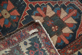 Vintage distressed Bakhtiari carpet corner with indigo, red, and beige geometric serrated lattice.