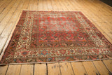 Distressed corner of antique Malayer rug, showing worn cranberry rose field and detailed ivory, sky blue borders.