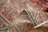 Folded Hamadan runner detail: distressed pile, brick red herati motif, meandering border, cream fringe.