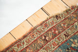 Frayed end of an antique Halvei Bijar rug, showing intricate red, beige, and blue border.