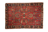 Distressed antique Sarouk rug; silky red wool with sprawling blue and black floral motifs.