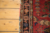 Antique Sarouk rug with black floral border, soft red field, and decorative distressed wool.