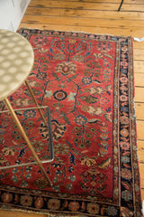 Distressed red field with intricate floral motifs and dark blue border on Sarouk rug.