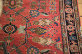 Distressed antique Sarouk rug's soft red pile and dainty floral motif, showing a dark border.