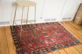Distressed antique Sarouk rug corner with bold red field and contrasting navy floral border.