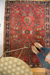 Distressed bold red field of the antique Sarouk rug with sprawling floral motifs.